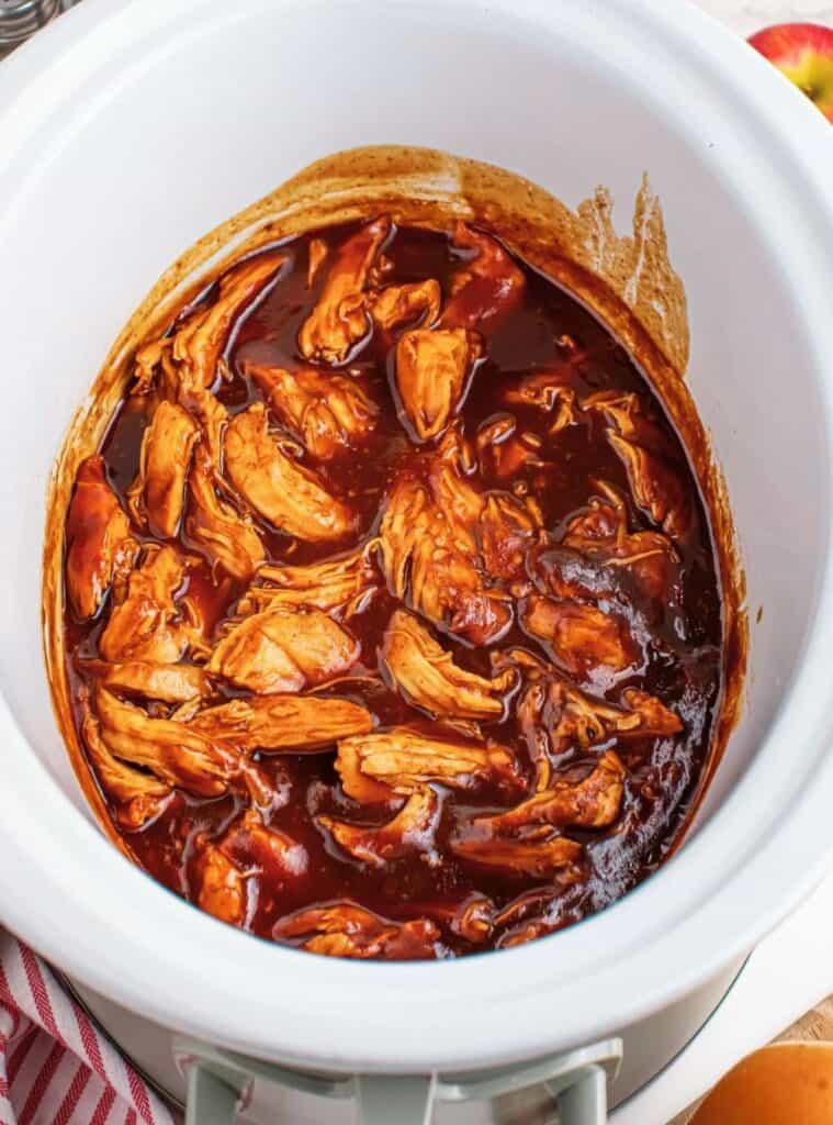 uicy crockpot pulled chicken with apple cider BBQ sauce piled high on a sandwich bun.