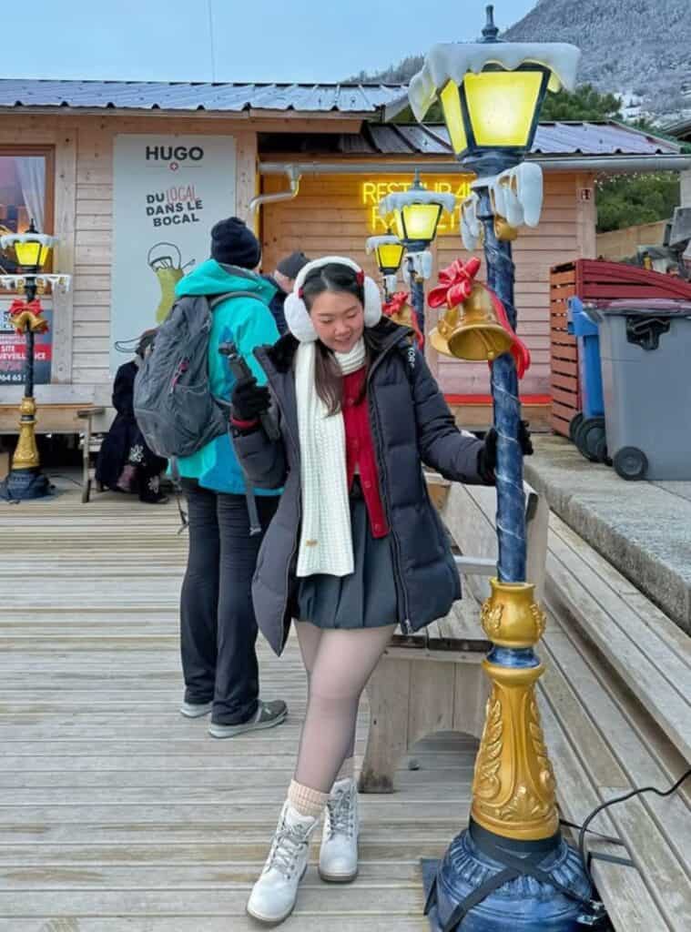 30 Black Long Puffer Jacket Red Cardigan Grey Pleated Mini Skirt White Lace up Boots black long puffer jacket layered with a red cardigan and mini skirt for winter outfits in snow